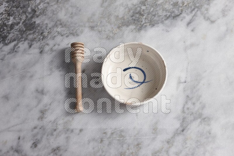 Multicolored pottery bowl with wooden honey dipper on the side on grey marble background