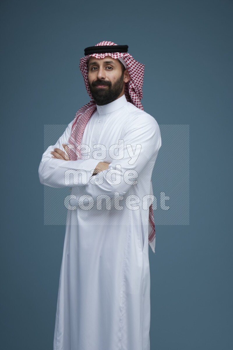 A man posing in a blue background wearing Saudi Thob and Shomag