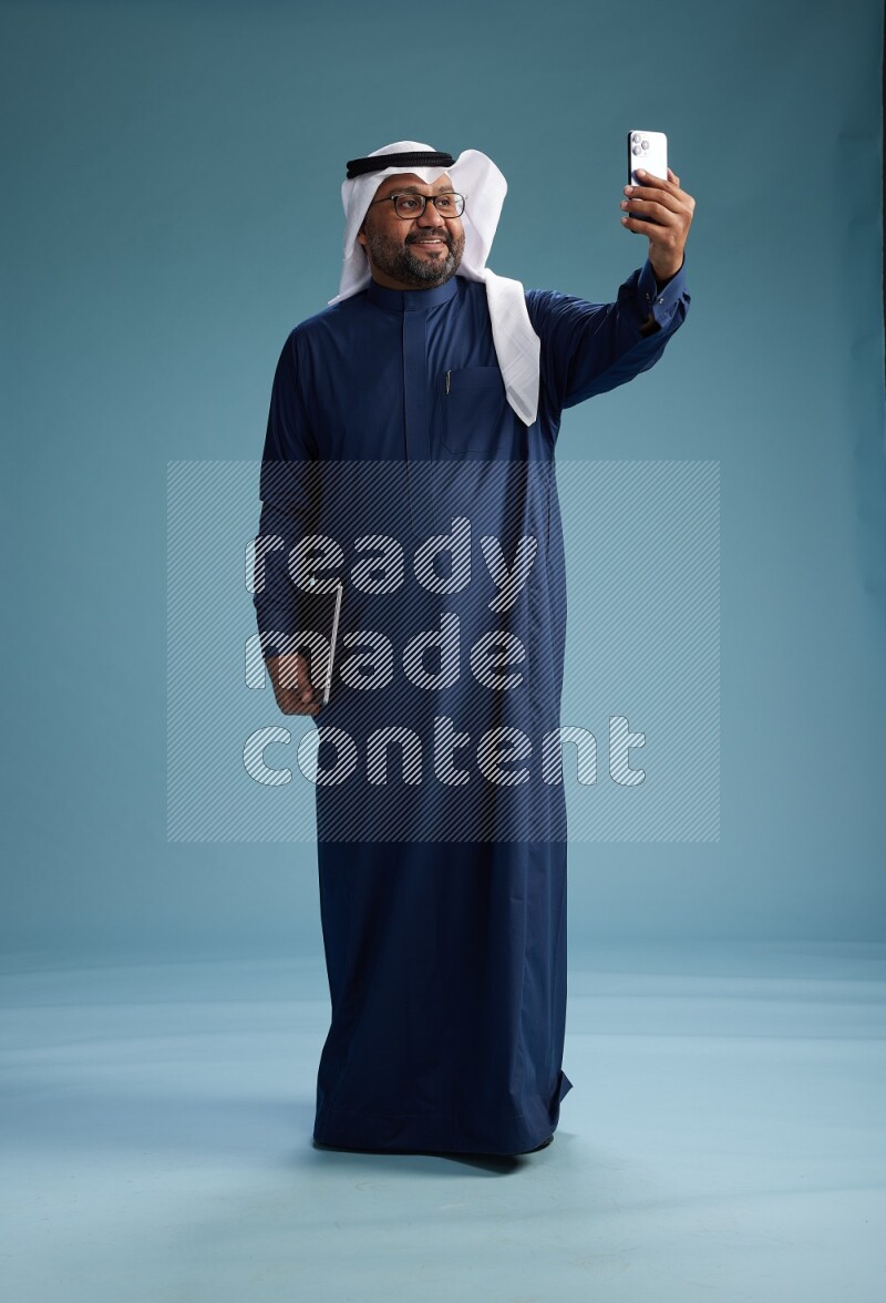 Saudi Man with shimag Standing taking selfie on blue background