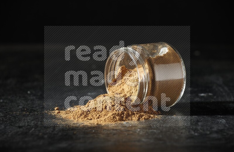 وعاء زجاجي مقلوب ممتلئ ببودرة بهار الفلفل الحلو والبودرة تناثرت منه على خلفية سوداء