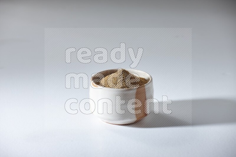 A beige bowl full of cumin powder on a white flooring