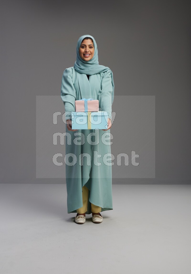 Saudi Woman wearing Abaya standing holding gift box on Gray background