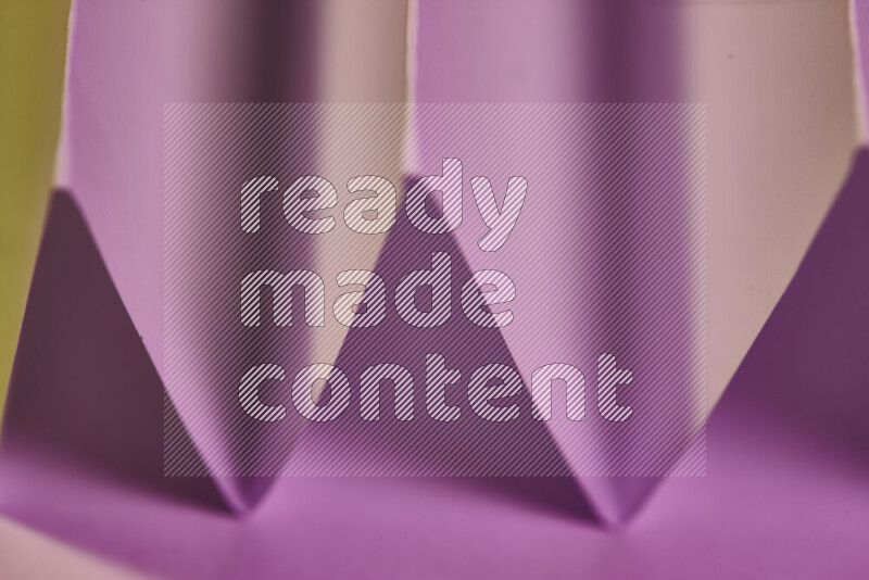 A close-up abstract image showing sharp geometric paper folds in pink gradients and warm tones