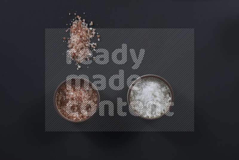 2 pottery bowls one is filled with himalayan salt and the other with white salt on black background
