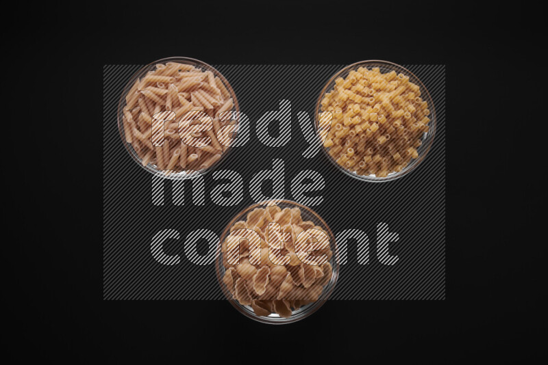 Different pasta types in glass bowls on black background