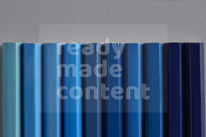 A collection of colored pencils arranged showcasing a gradient of blue hues on grey background