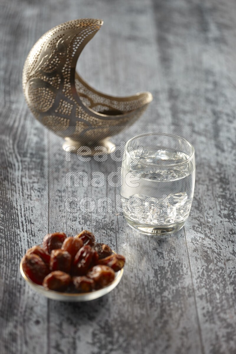 A silver lantern with different drinks, dates, nuts, prayer beads and quran on grey wooden background
