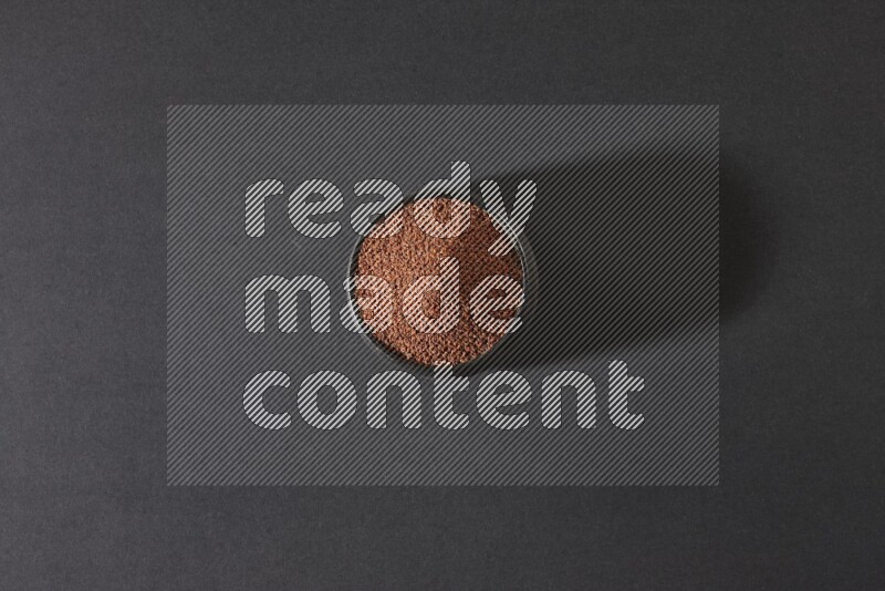 A black pottery bowl full of garden cress seeds on a black flooring
