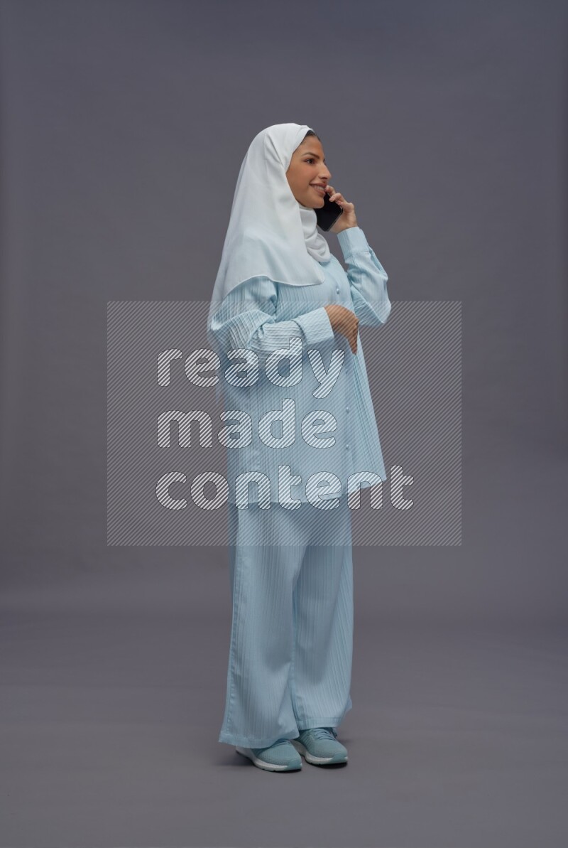 Saudi woman wearing hijab clothes standing talking on phone on gray background