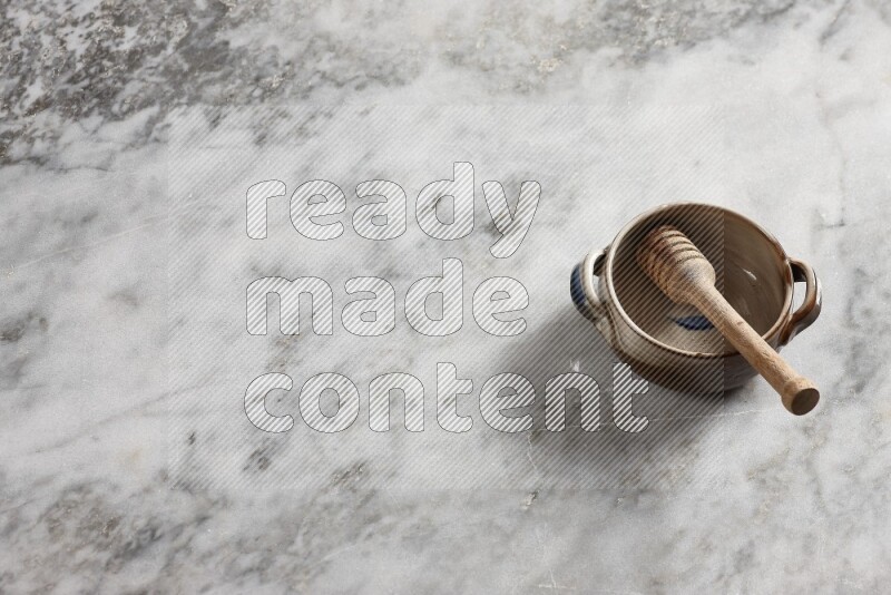 Multicolored pottery bowl with wooden honey dipper in it on grey marble background