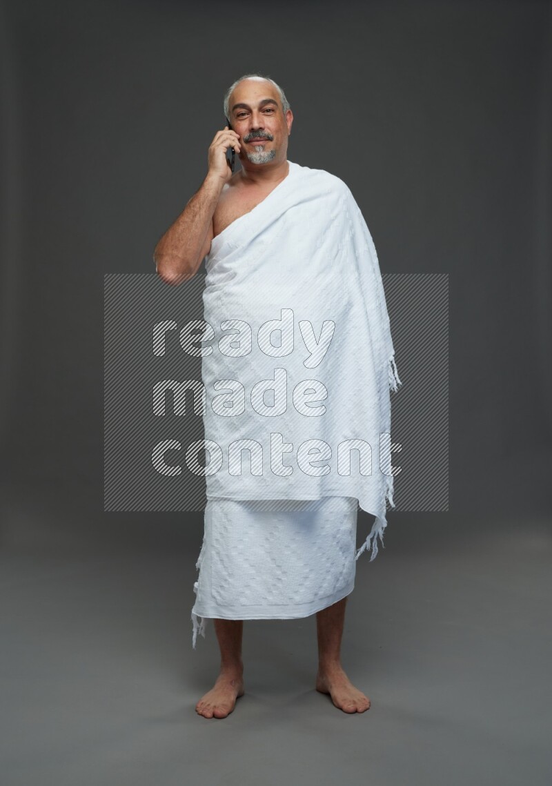 A man wearing Ehram Standing talking on phone on gray background