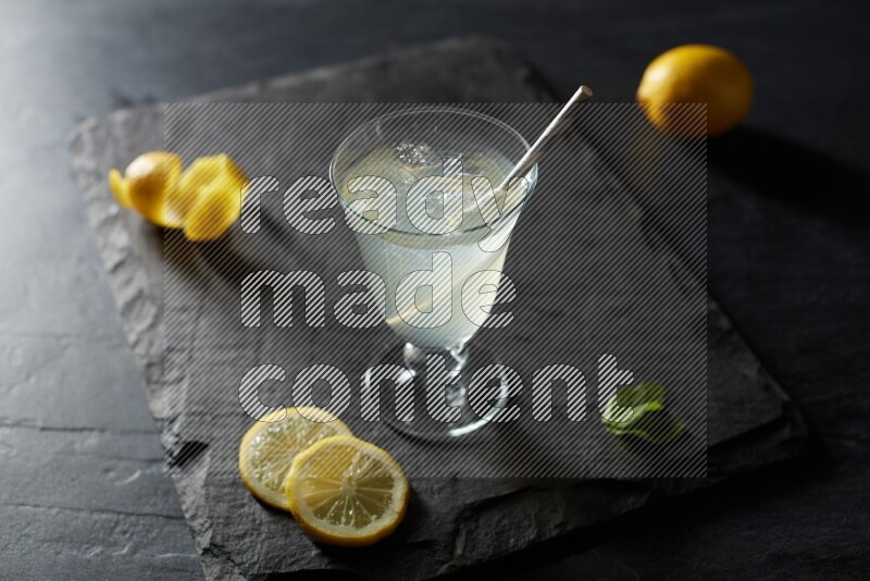 A glass of lemon juice with a straw on black background