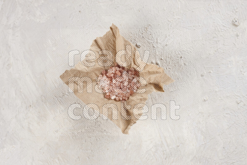A crumpled piece of paper full of pink himalayan salt on white background