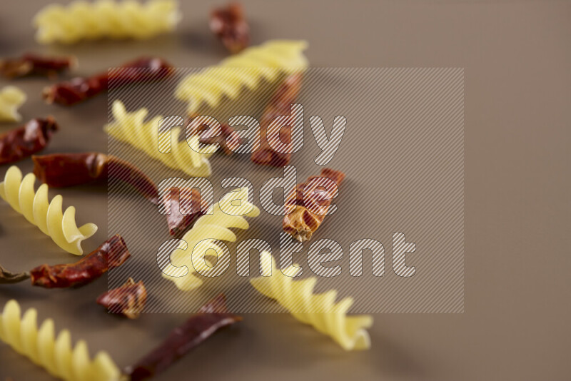 Raw pasta with different ingredients such as cherry tomatoes, garlic, onions, red chilis, black pepper, white pepper, bay laurel leaves, rosemary and cardamom on beige background