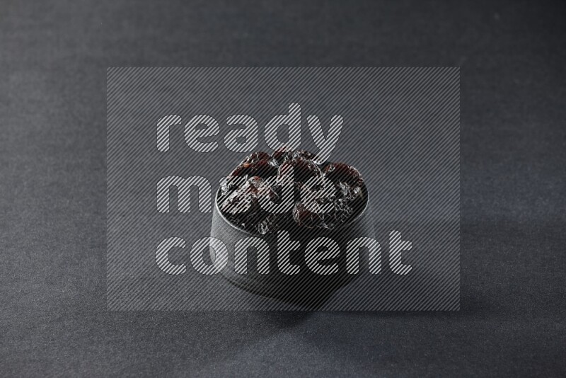 A black pottery bowl full of dried plums on a black background in different angles
