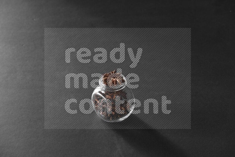 A glass spice jar full of star anise on black flooring