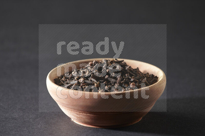 A wooden bowl full of cloves on a black flooring