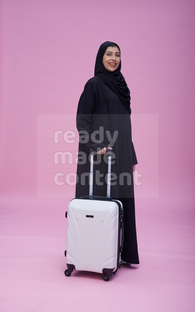 Saudi woman wearing Abaya standing holding bag on pink background