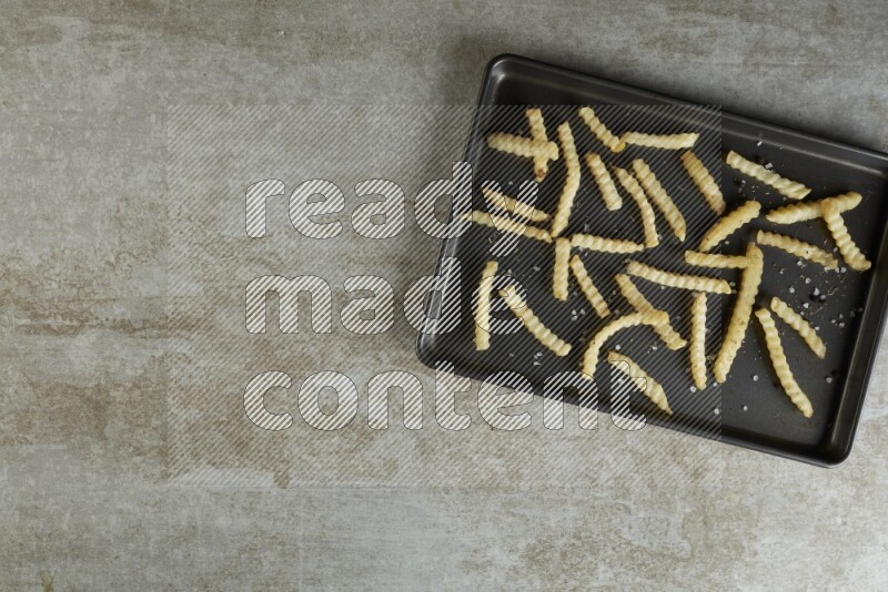 crinkle fries in a black stainless steel rectangle tray on grey textured counter top