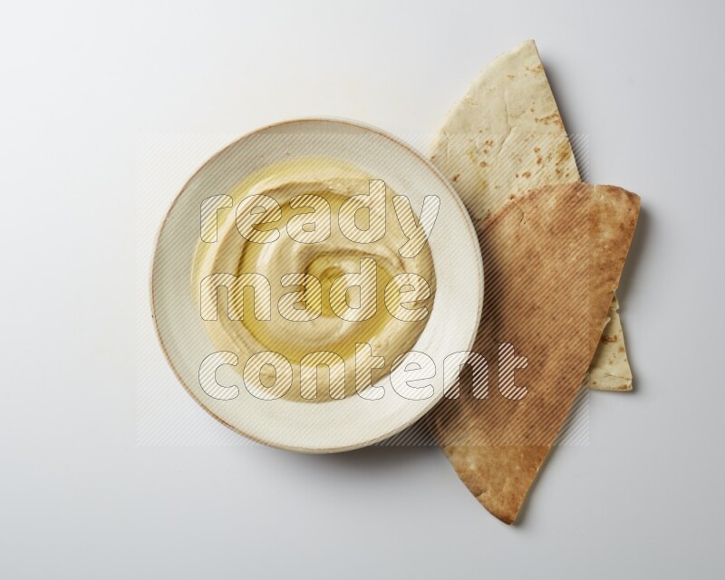 Hummus in a pottry plate garnished with olive oil on a white background