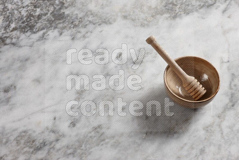 Beige pottery bowl with wooden honey dipper in it on grey marble background