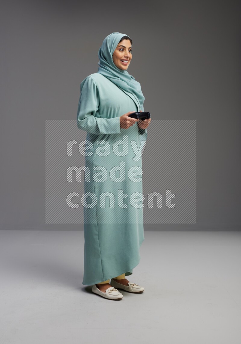 Saudi Woman wearing Abaya standing Playing Games on Gray background