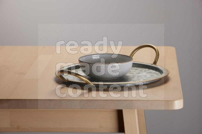 multicolored bowl placed on a rounded stainless steel tray with golden handels on the edge of wooden table