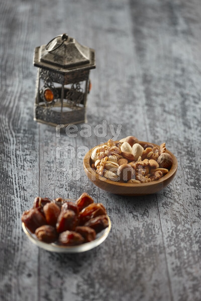 A silver lantern with different drinks, dates, nuts, prayer beads and quran on grey wooden background