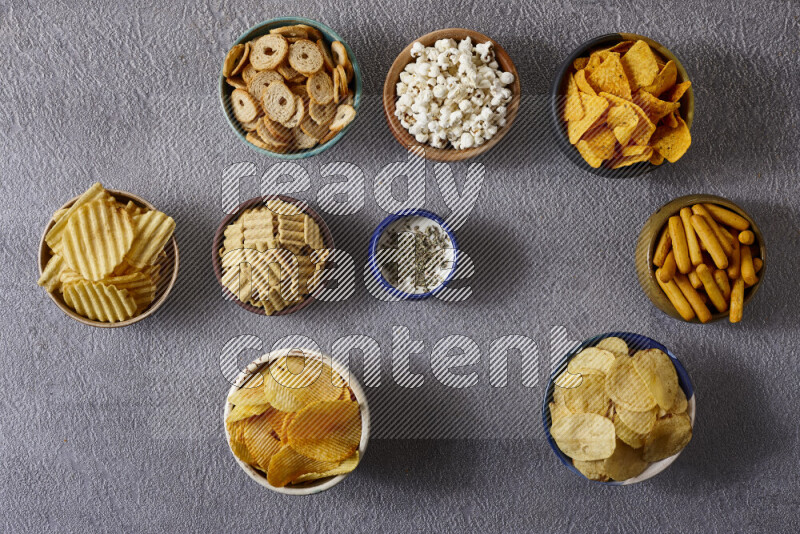 Assorted snacks in pottery bowls on grey background
