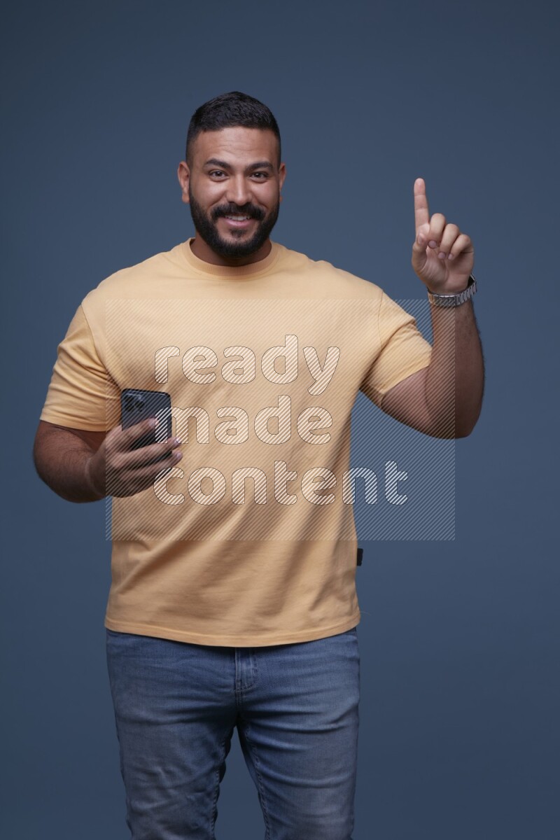 A man Pointing at a Smartphone on Blue Background wearing Orange T-shirt