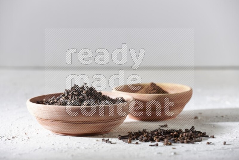 2 wooden bowls full of cloves powder and whole cloves on a textured white flooring