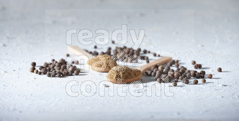 Wooden spoons full of allspice powder and allspice whole balls spreaded on a textured white flooring