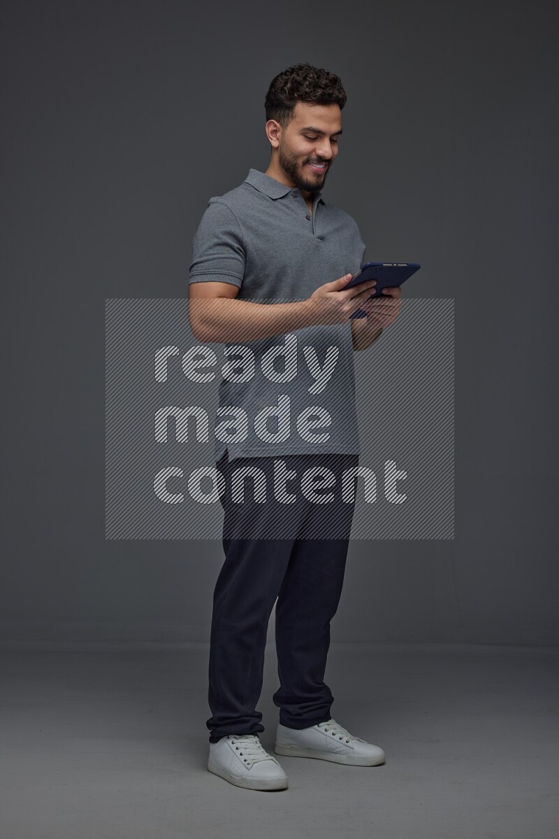 A man wearing casual standing and using his tablet and making multi hand gestures different angles eye level on a gray background
