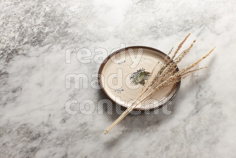 Wheat stalks on decorative pottery plate on grey marble background