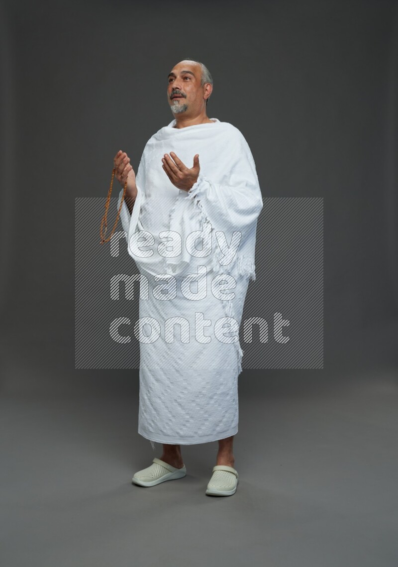 A man wearing Ehram Standing dua'a on gray background