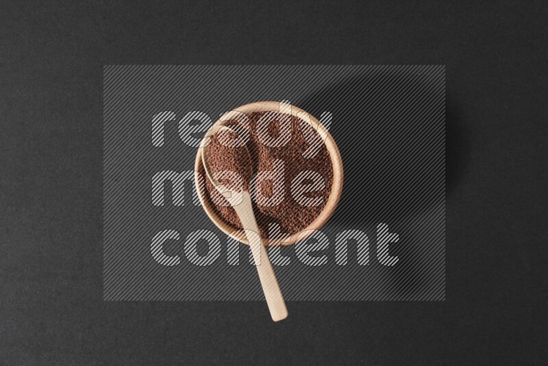 A wooden bowl full of garden cress seeds and a wooden spoon full of the seeds on it on a black flooring