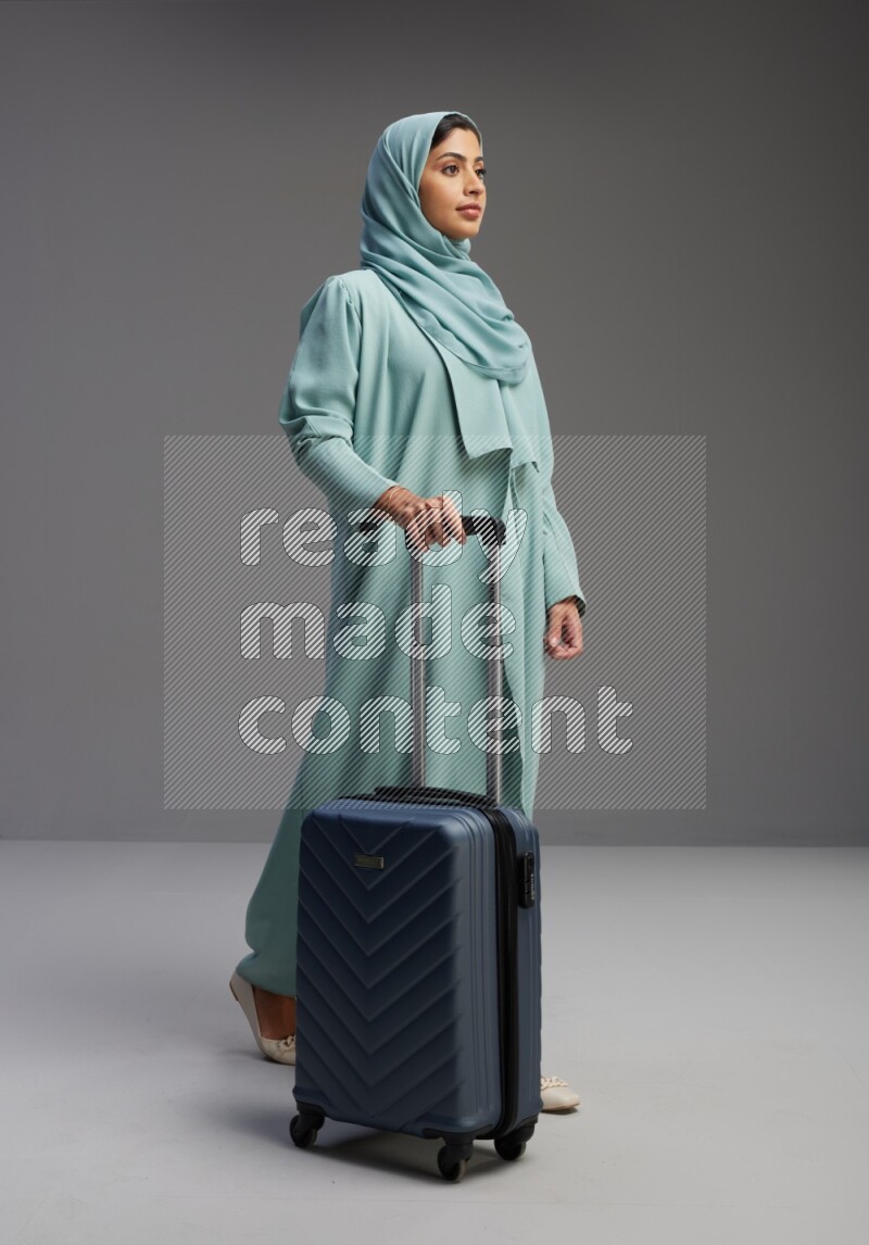 Saudi Woman wearing Abaya standing holding Travel bag on Gray background
