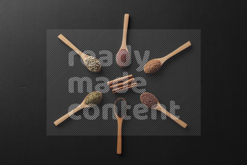 wooden spoons filled with white peppers, mustard seeds, black seeds, garden cress, cumin and flax on black flooring and shaped like a clock