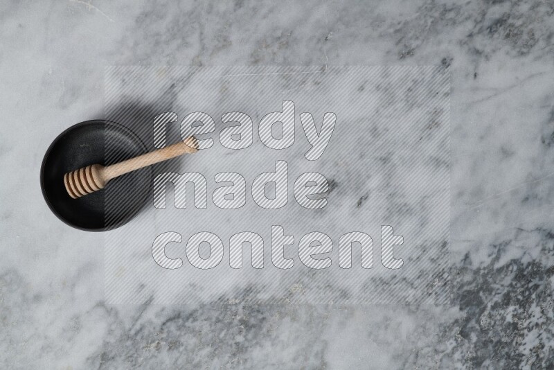 Black pottery bowl with wooden honey dipper in it on grey marble background