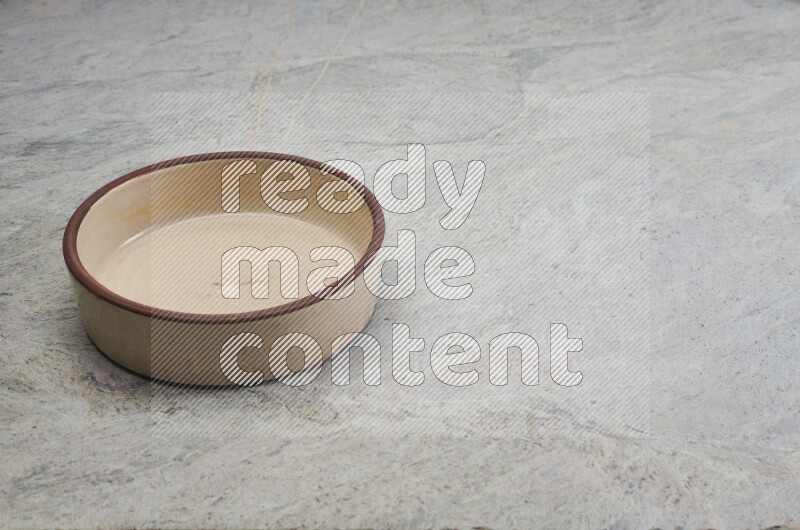 A beige pottery oven bowl on grey marble background