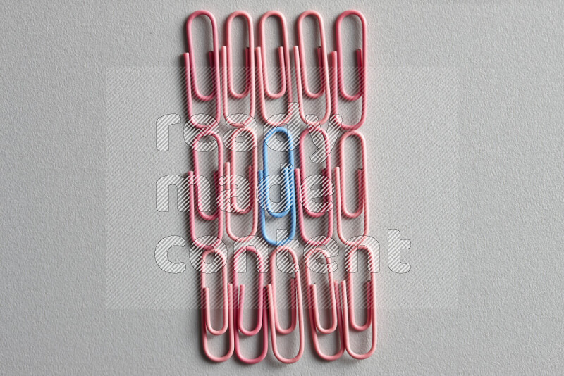 A bunch of pink paper clips with a different colored paper clip in the center on grey background