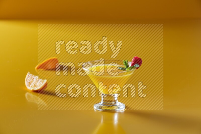 glass of orange juice with berry & mint on yellow background