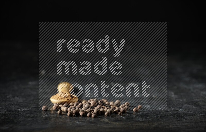 A wooden spoon full of allspice powder and whole balls spreaded on a textured black flooring