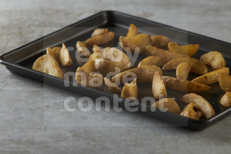 wedges potato in a black stainless steel rectangle tray on grey textured counter top