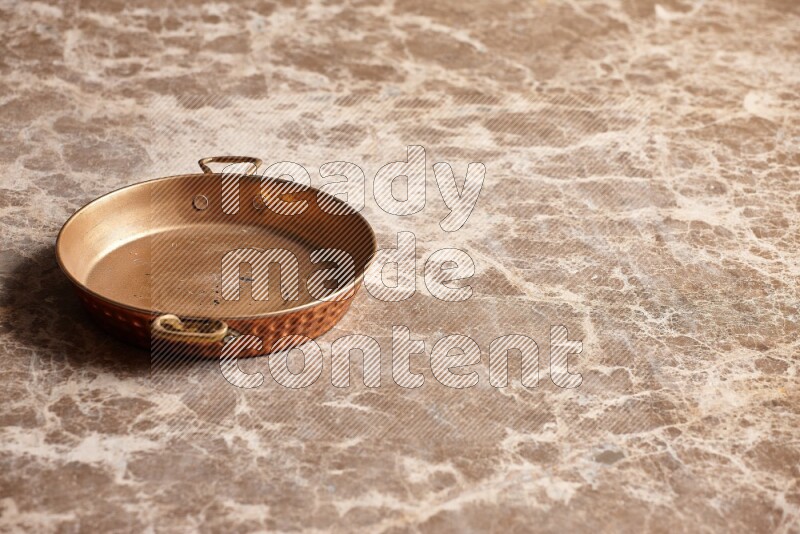 A small copper pan on beige marble background