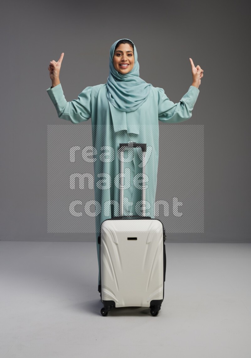 Saudi Woman wearing Abaya standing holding Travel bag on Gray background