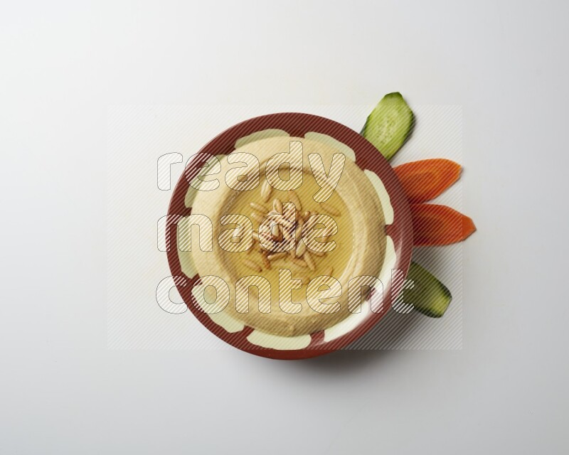 Hummus in a traditional plate garnished with pine nuts on a white background