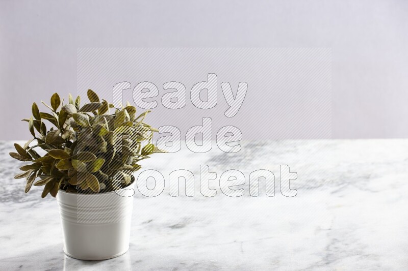 Green artificial plant in white pot on light grey marble background