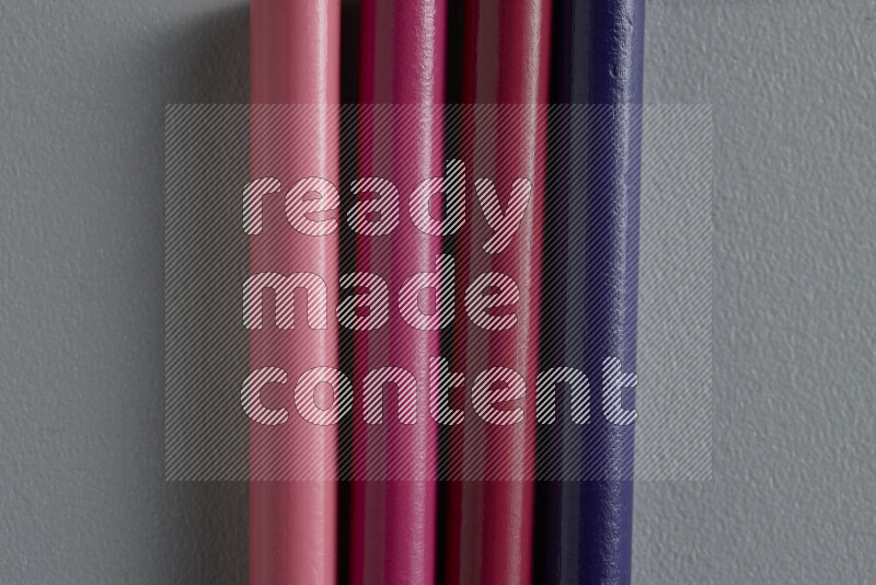 A collection of sharpened colored pencils arranged showcasing a gradient of pink and purple hues on grey background