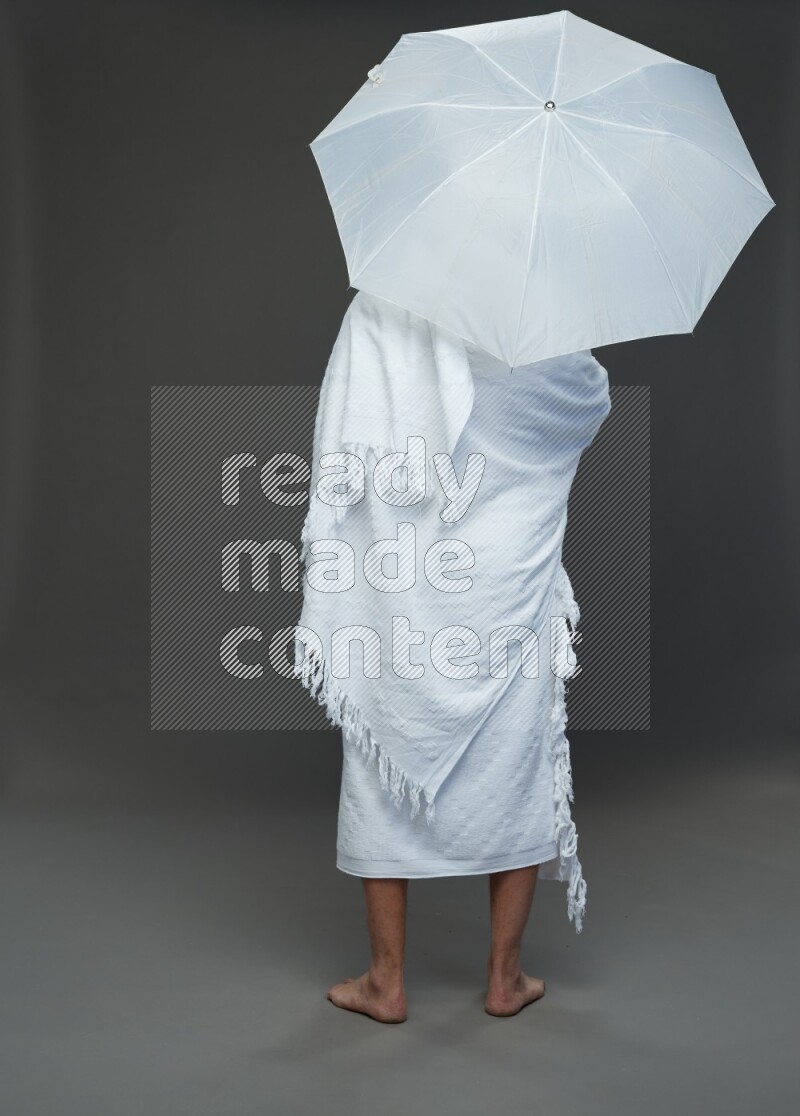 A man wearing Ehram Standing holding umbrella on gray background